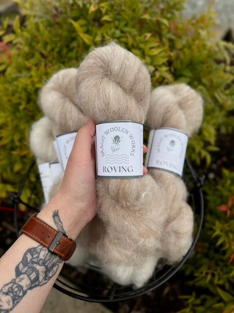 Hand holding a light warm brown hank of Icelandic and alpaca roving, above a basket of more hanks.