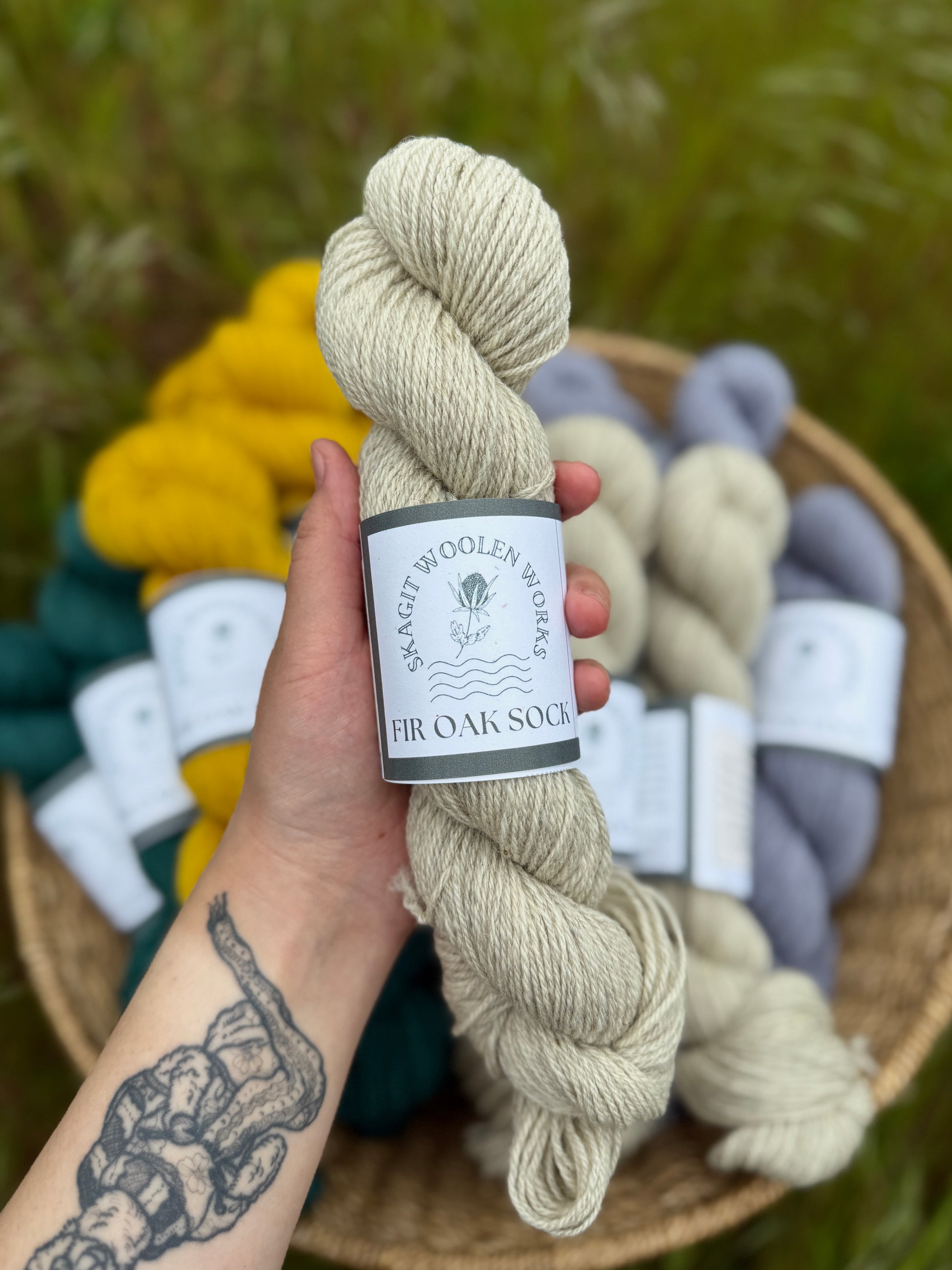 Hand holding a skein of natural creamy grey Romney x Suffolk sock yarn.