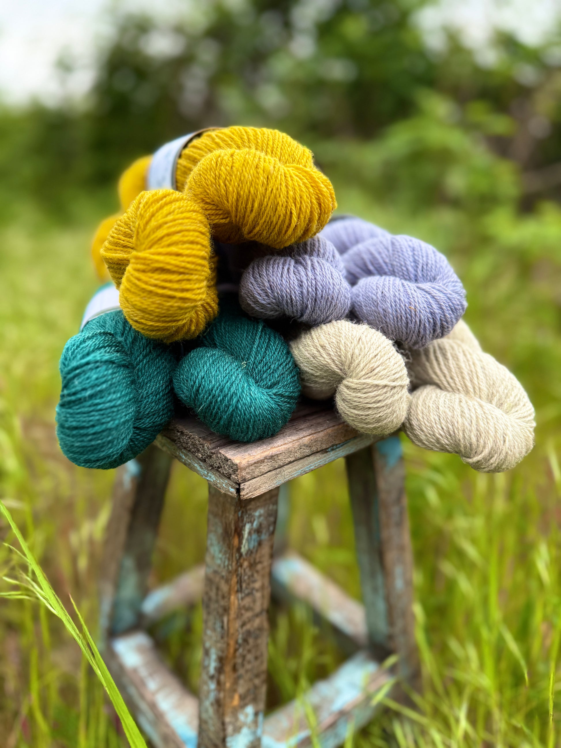 All 4 colorways of Romney Suffolk cross yarn stacked on a weathered wooden stool.